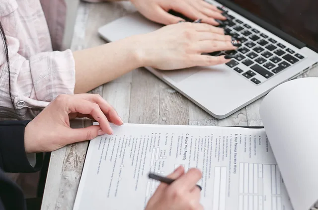 Close-up of hands typing on a laptop and reviewing business documents, focused on finance and legal tasks. How SBA loans fund marketplace startup revenue models in Texas